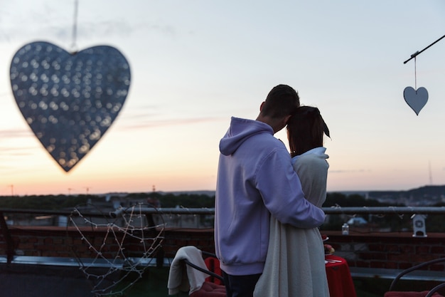 Free photo boy and girl hug each other tender standing on the rooftop in the rays of evening lights