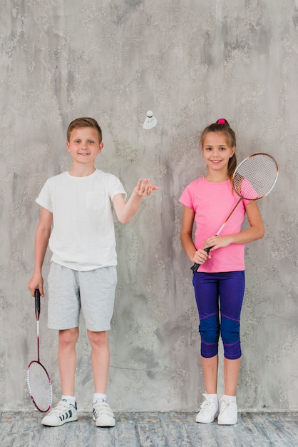 Boy and girl players with rackets and shuttlecock against concrete backdrop