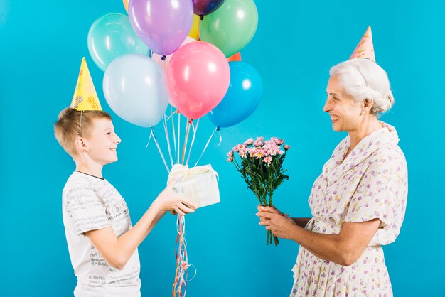 Boy giving birthday gift to happy grandmother on blue background