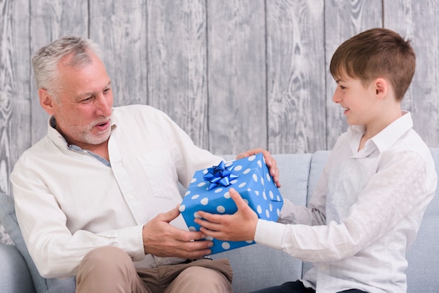 Boy giving blue wrapped birthday gift box to his grandfather