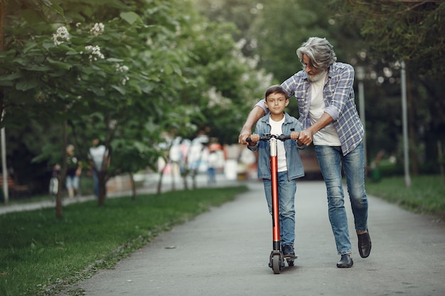 Boy and grandfather are walking in the park. Old man playing with grandson. Child with scooter.