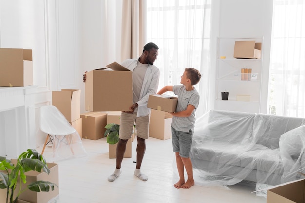 Free Photo boy helping his father to carry packages for moving out