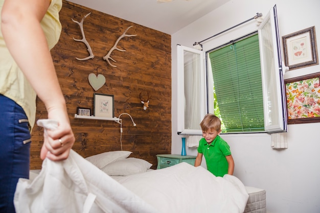 Free Photo boy helping mother to make bed