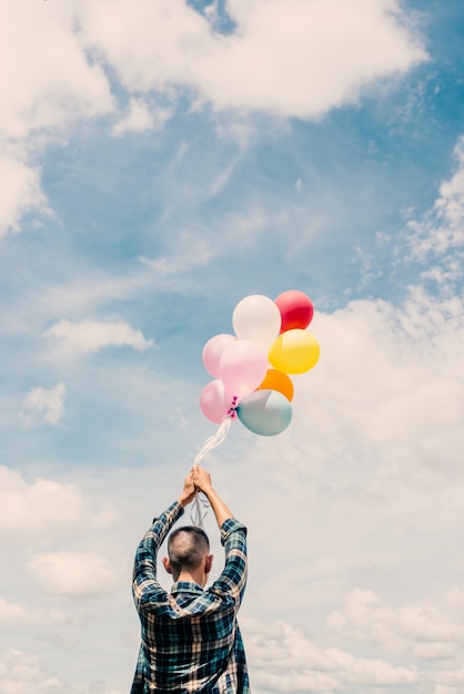 Free photo boy holding colorful balloons with sky background