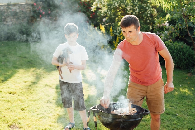 Free Photo boy holding dog standing near his father preparing food in park