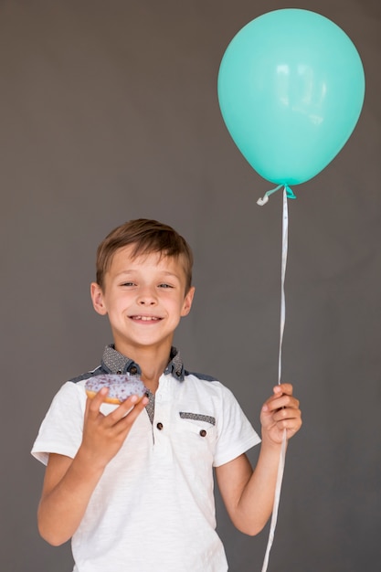 Free Photo boy holding a glazed doughnut and a balloon