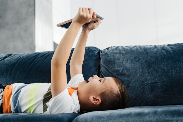 Boy a home laying on the couch and using digital tablet