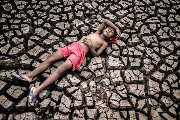 Free photo the boy lay flat, laying his hands on the belly and forehead on dry soil.