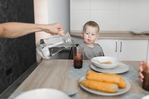 A boy looking at a person pouring water in the glass at breakfast