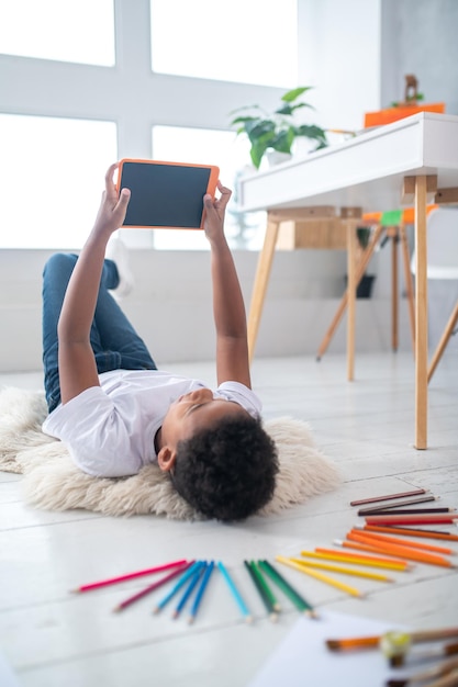 Free Photo boy lying on floor taking selfie on tablet