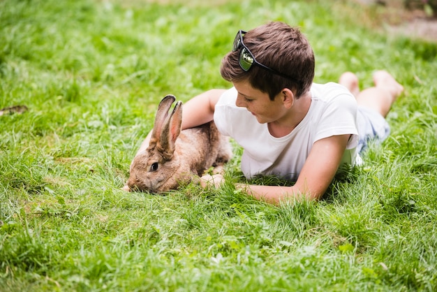 Boy lying with his pet rabbit on green grass