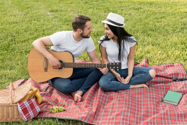 Boy playing the guitar for his girlfriend on a picnic blanket