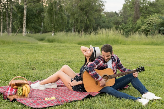 Boy playing the guitar for his girlfriend on a picnic blanket