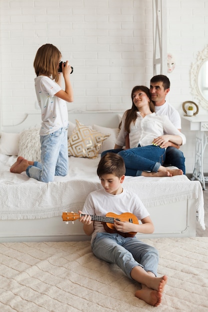 Boy playing ukulele in front of his sister taking picture of their parents