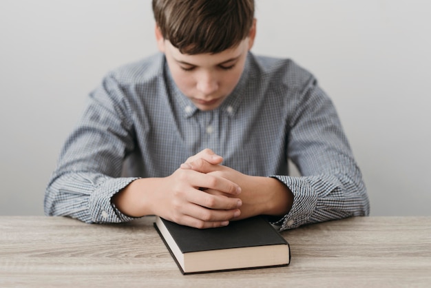 Free photo boy praying with his hands on a bible