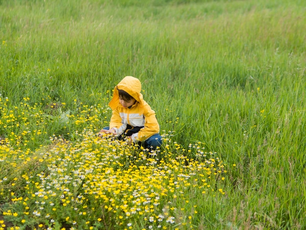 Boy in raincoat picking flowers long shot