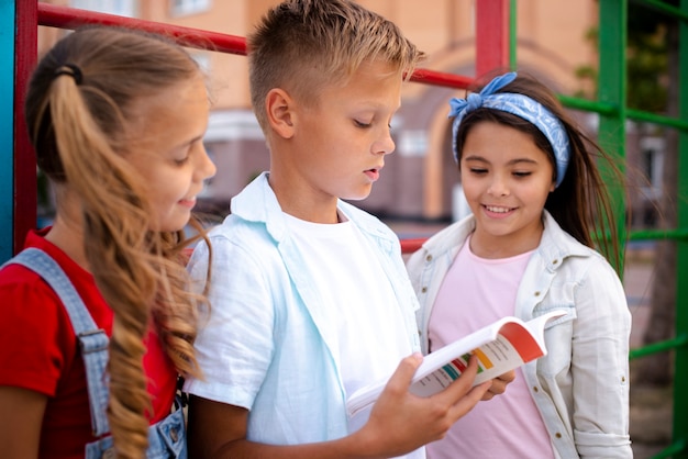 Boy reading from a book with two girls