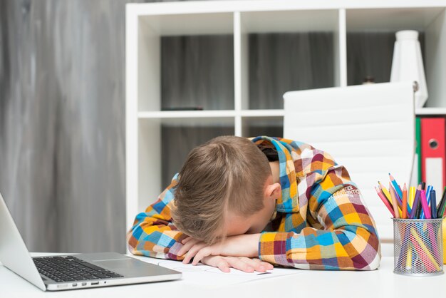 Boy sleeping in front of laptop on desk