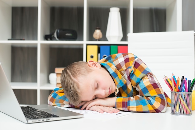 Free photo boy sleeping in front of laptop on desk