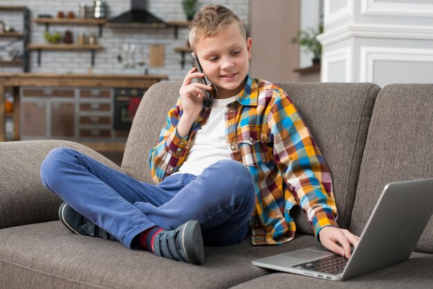 Boy using laptop on couch and making phone call