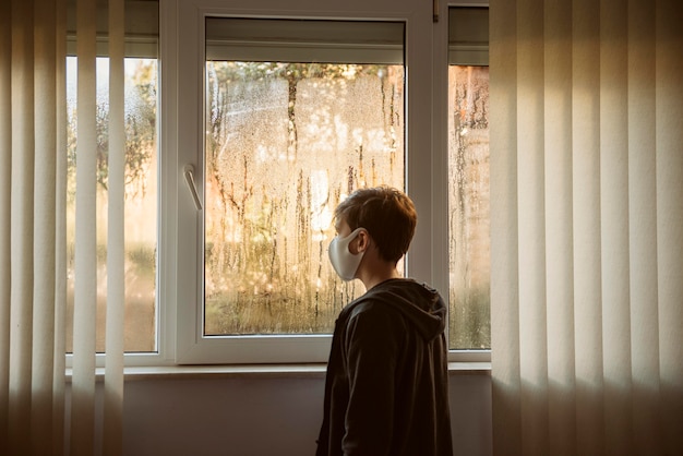 Boy with face mask standing next to windows