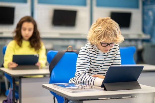 Boy with glasses looking at tablet sitting at desk