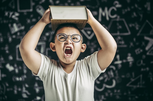 Free photo a boy with glasses studied and put a book on his head in the classroom.