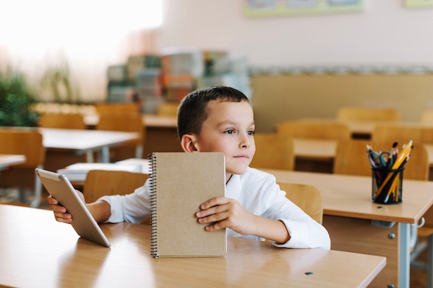 Free Photo boy with tablet and notepad at table