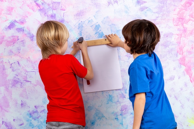 Free photo boys back view working with hammer in red and blue t-shirts on colorful wall