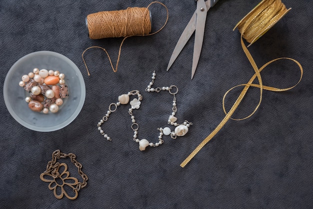 Free photo bracelet made with yarn spool; beads; scissor and golden ribbon on black textured backdrop