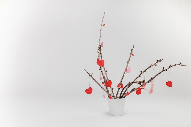 Free Photo branches of a plant in a white flowerpot with hanging hearts