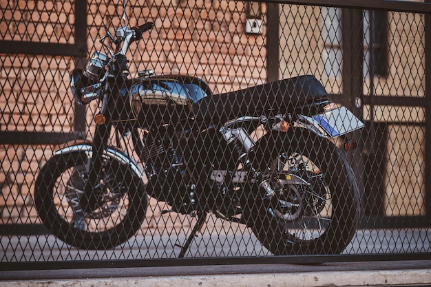 Free photo brand new, shiny black retro chopper is parked next to brick building, behind the fence.