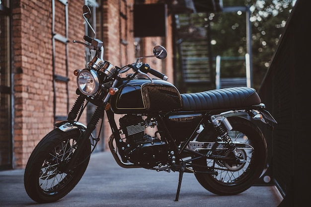 Free photo brand new, shiny black retro chopper is parked next to brick building.