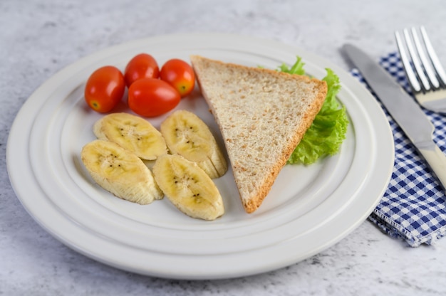 Free Photo bread, banana, and tomato on white plate with fork and a knife.