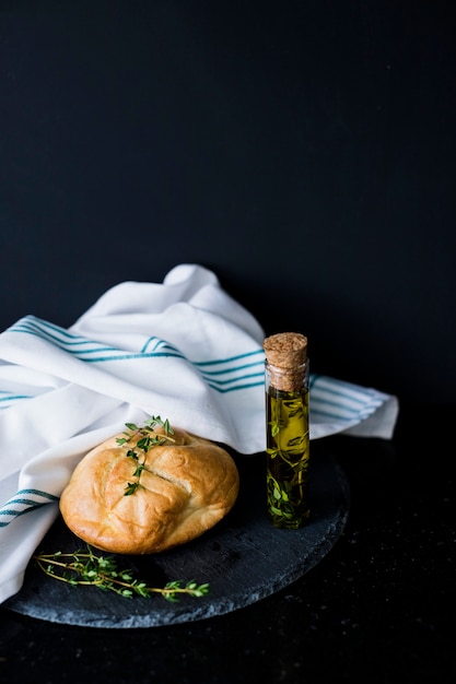 Free photo bread bun; thymes; olive oil and white napkin on slate against black background