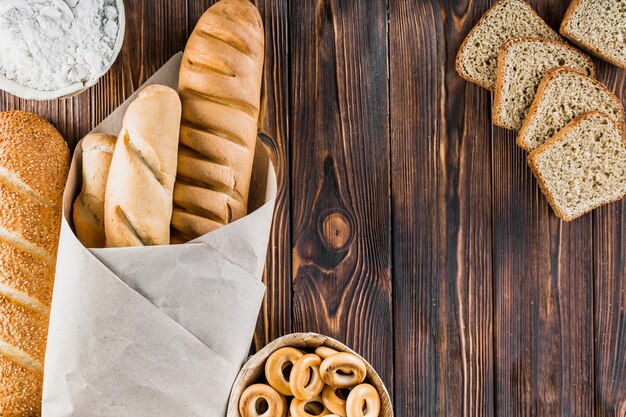 Bread slice, baguettes, bagels, flour on the wooden backdrop