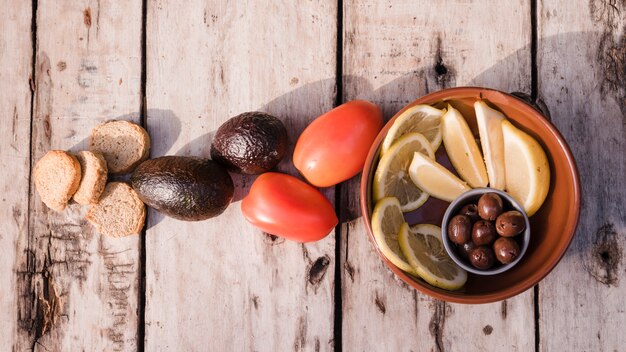 Bread slices; avocado; tomatoes olives and orange slices on table