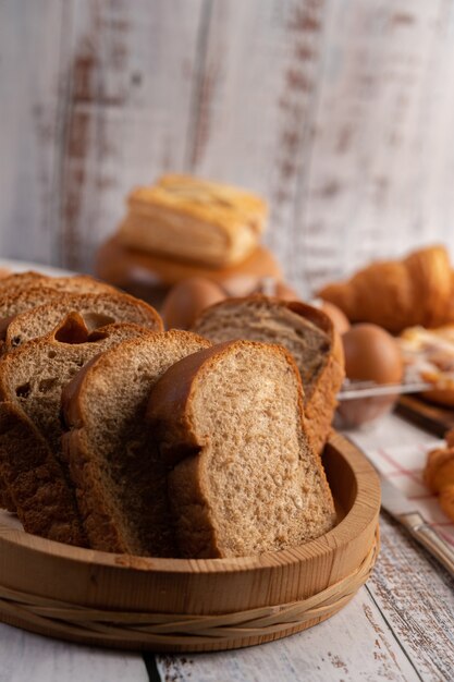 Bread slices placed in a wooden plate on a white wooden table.