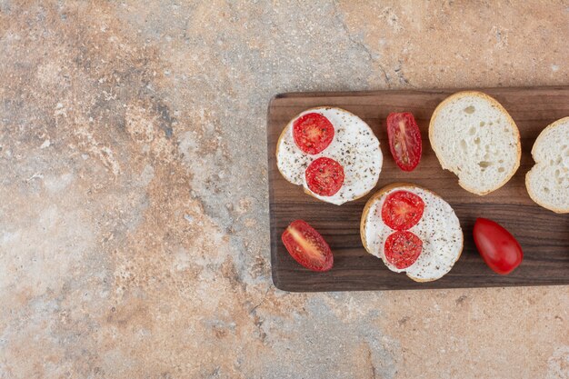 Bread slices with cream and tomato on wooden board