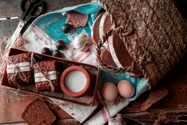 Free photo bread slices wrapped with white paper and thread, milk pot inside a boc, basket around.top view.