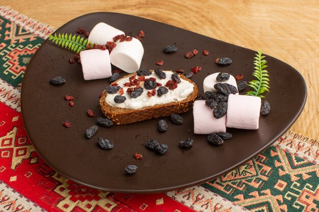 bread toast along with marshmallows and dried fruits inside dark plate on wood