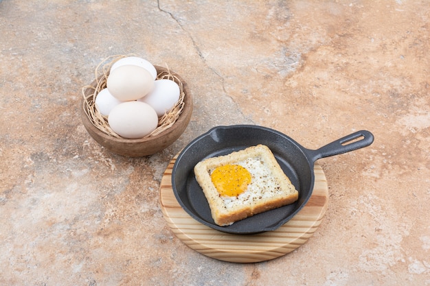 Bread with fried eggs on black pan with bowl of eggs