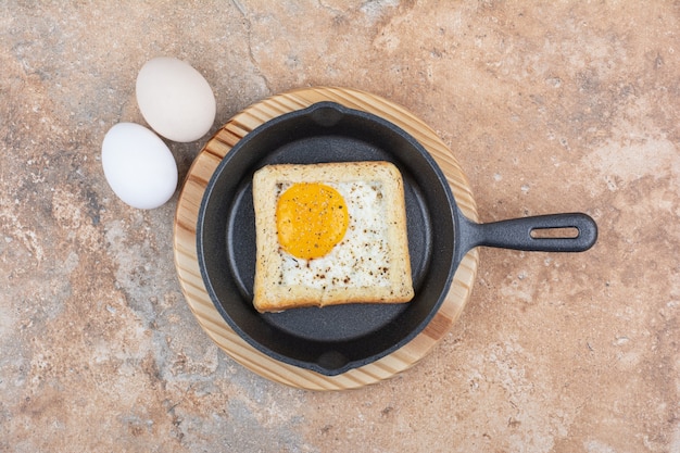 Free Photo bread with fried eggs on black pan with raw eggs