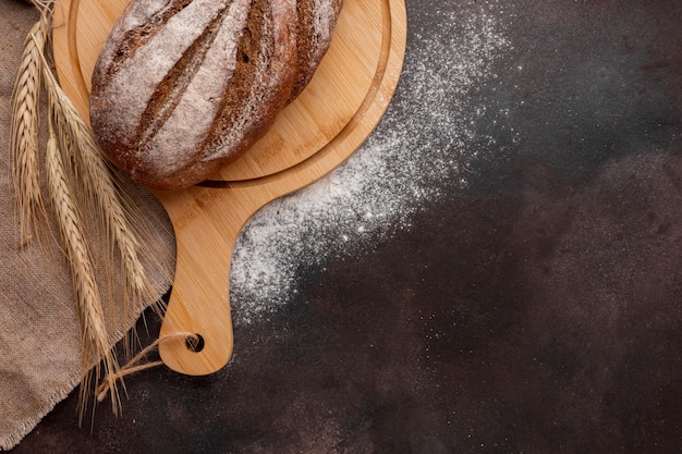 Bread on wooden board with wheat grass and flour