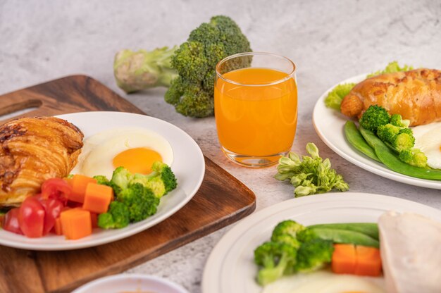 Breakfast consists of chicken, fried eggs, broccoli, carrots, tomatoes and lettuce on a white plate.