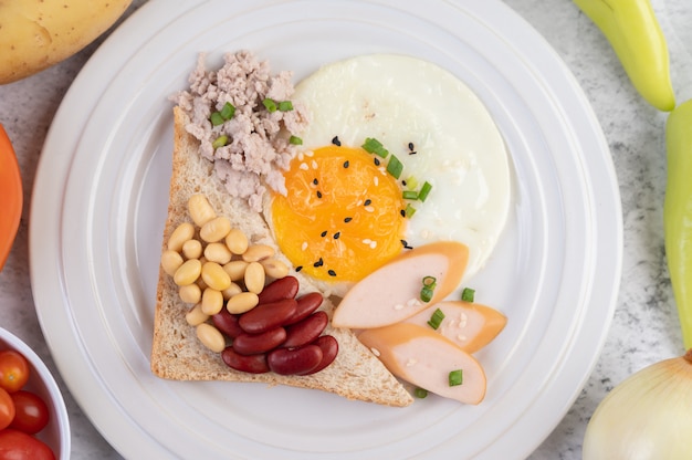 Breakfast consists of fried eggs, sausage, minced pork, bread, red beans and soy on a white plate.