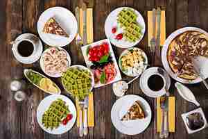 Free photo breakfast food table. festive brunch set, meal variety with spinach waffles, salmon, cheese, olives, chicken rolls and cheesecake. top view. flat lay