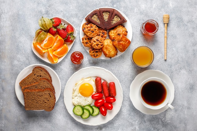 A breakfast plate containing cocktail sausages,fried eggs,cherry tomatoes,sweets,fruits and a glass of peach juice.