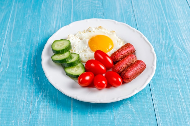 Free photo a breakfast plate containing cocktail sausages,fried eggs,cherry tomatoes,sweets,fruits and a glass of peach juice.