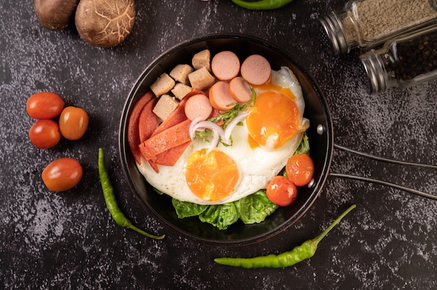 Breakfast with fried eggs, sausage, and ham in a pan with tomatoes. Chili and basil.